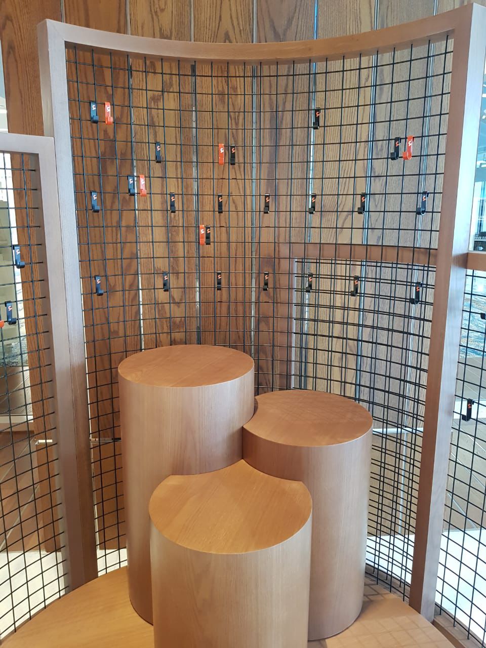 Three wooden cylindrical stools in front of a grid wall with hanging items.